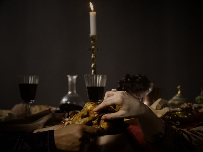 Two people sharing a piece of bread at a candlelit table, with wine glasses and a bottle in the background.