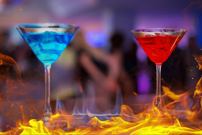 Two colorful cocktails, one blue and one red, on fire with a blurred background.