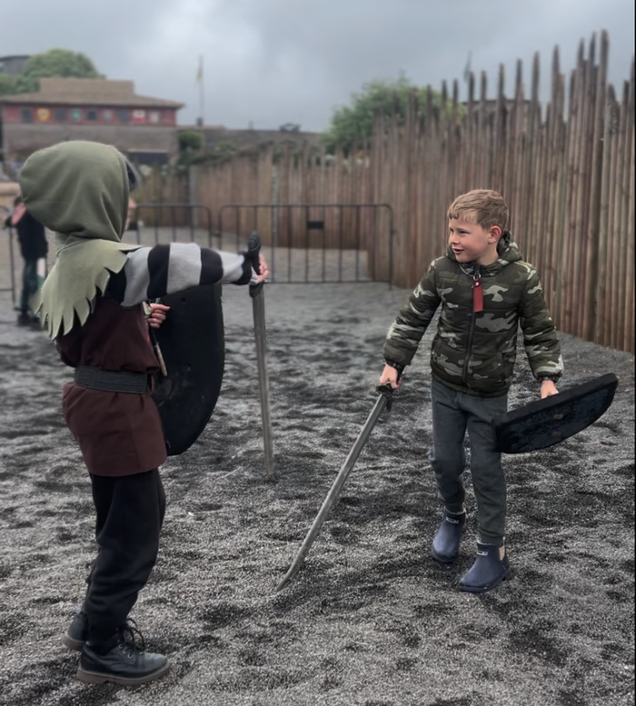Two children playing with toy swords and shields in an outdoor setting.